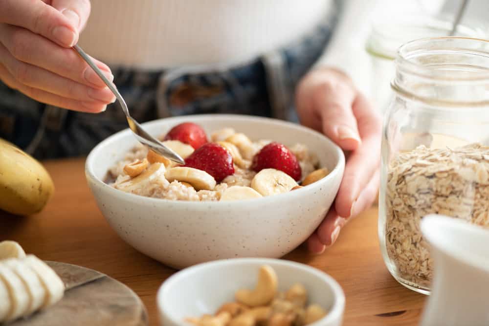 Woman eating oatmeal porridge with fruits. Concept of healthy lifestyle and dieting. Warm morning light, healthy breakfast on wooden table